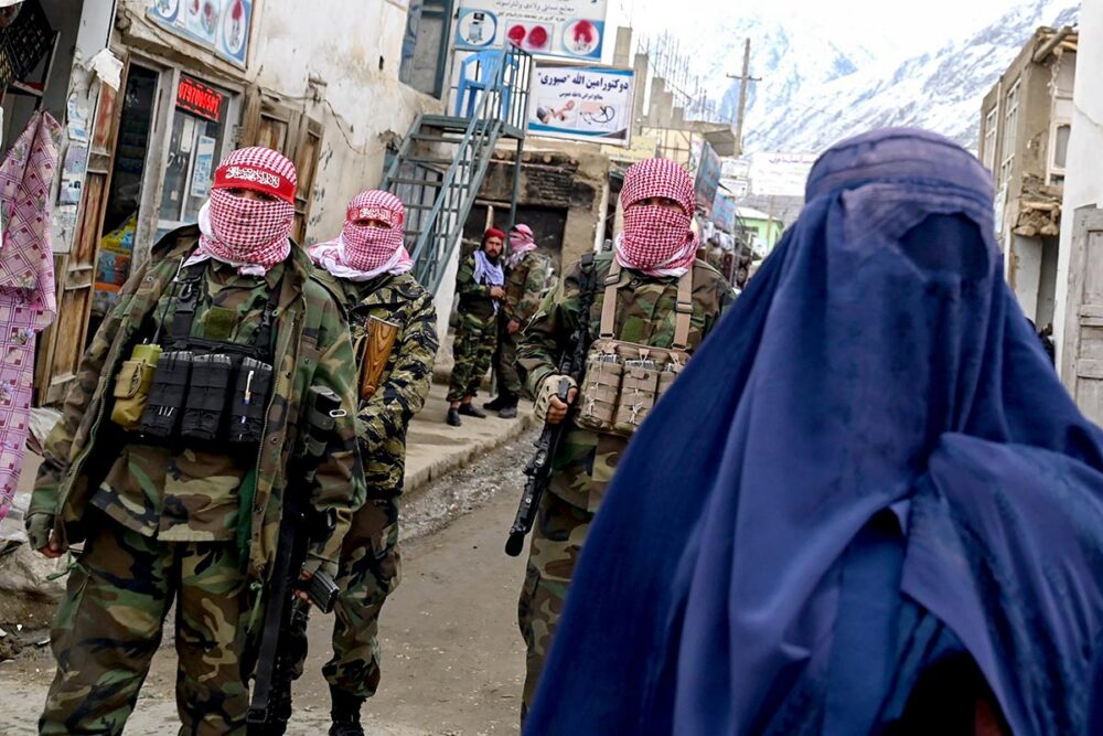 Gender apartheid for women in Iran and women in Afghanistan - Photo: a woman wearing a hijab walks down a street, closely followed by a Taliban patrol.