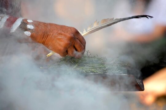 En Australie la justice transitionnelle est mise à mal par la politique. La communauté aborigène tente de s’adapter aux défaillances des commissions vérité suite au récent changement de gouvernement dans le Queensland. Photo : un Aborigène, dont on ne voit que les mains, fait brûler des herbes lors d’une cérémonie traditionnelle de la fumée.