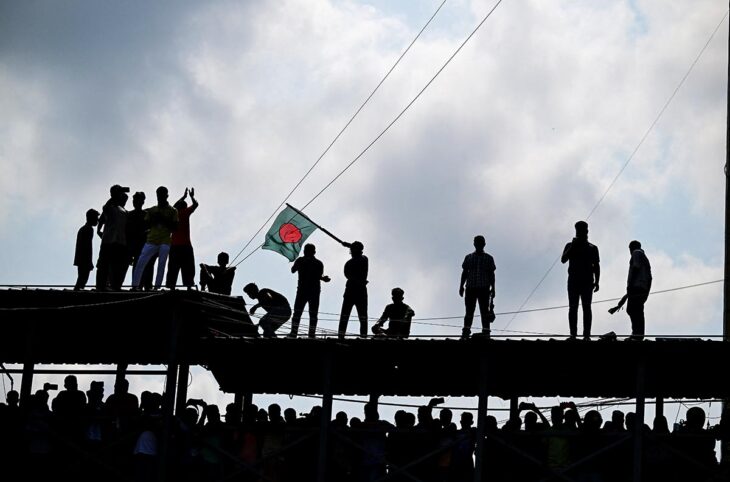 In Bangladesh, following the demonstrations in the summer of 2024 that led to mass crimes, the International Crimes Tribunal is back in action to try those responsible. But there are reports of concern about the operation of the local justice system and its politicisation. Photo: Demonstrators, seen against the light, stand on a high structure, one of them waving a Bangladeshi flag.