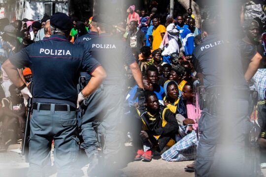 How does justice work in Italy for crimes committed against migrants? Photo: Migrants from Africa, most of whom pass through Libya, are rounded up and watched over by Italian police officers.