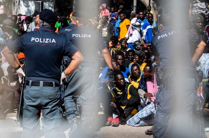 How does justice work in Italy for crimes committed against migrants? Photo: Migrants from Africa, most of whom pass through Libya, are rounded up and watched over by Italian police officers.