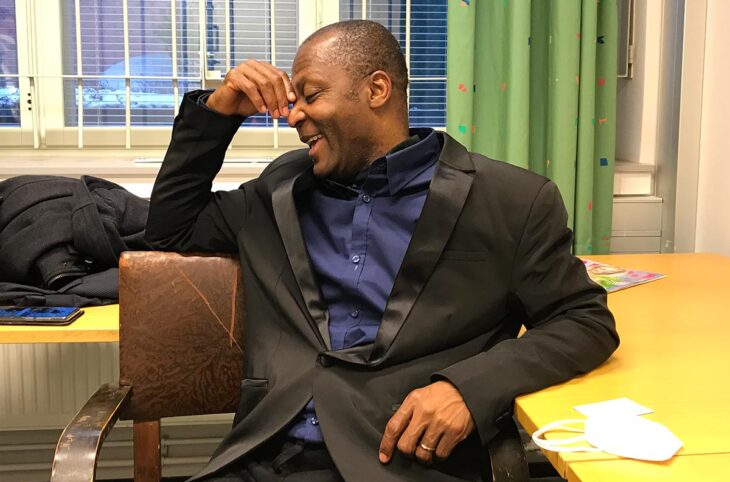 Acquitted twice in Finland on charges of war crimes in Liberia, Gibril Massaquoi is claiming more than 800,000 euros in financial compensation. Photo: Massaquoi, wearing a dark suit, laughs during an interview with Justice Info.