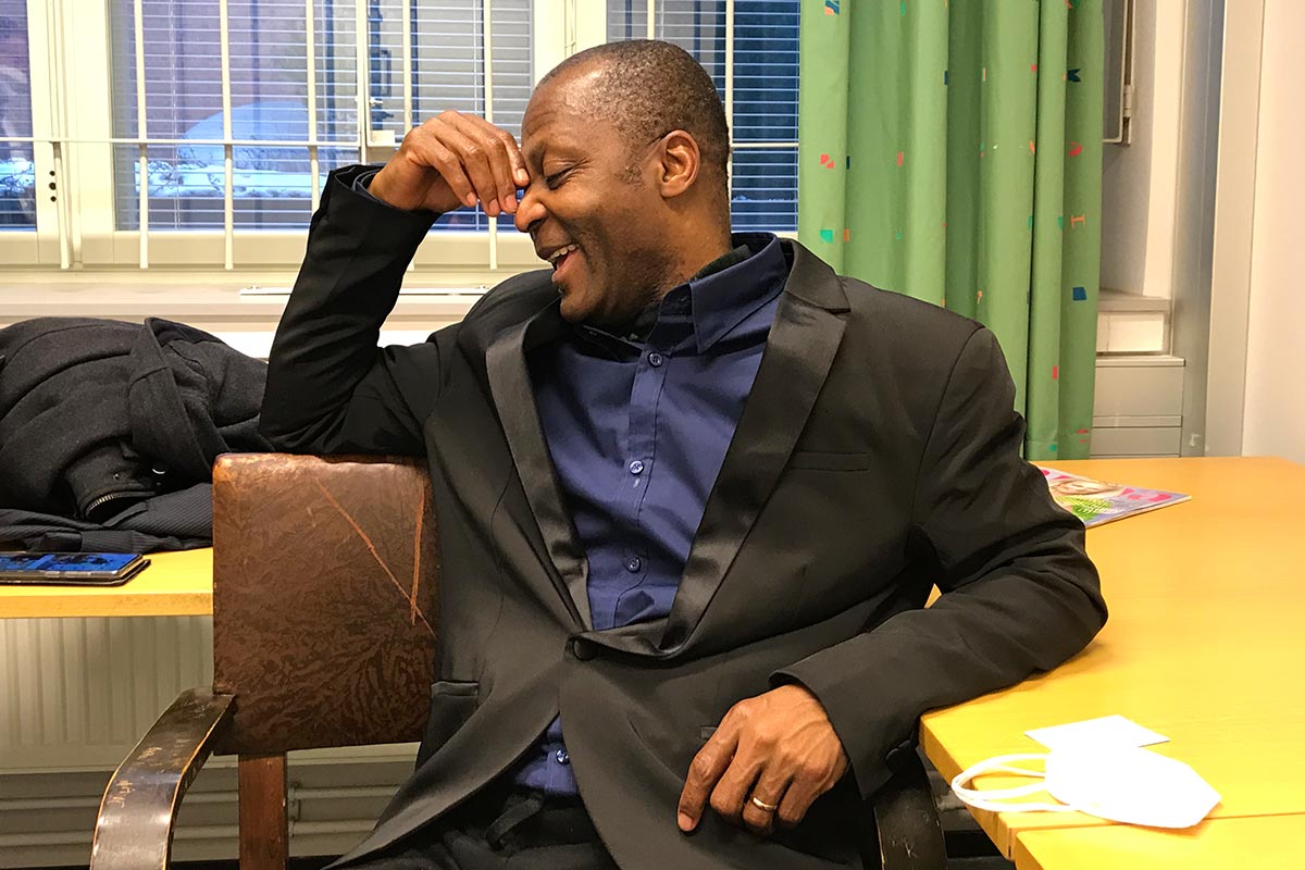 Acquitted twice in Finland on charges of war crimes in Liberia, Gibril Massaquoi is claiming more than 800,000 euros in financial compensation. Photo: Massaquoi, wearing a dark suit, laughs during an interview with Justice Info.