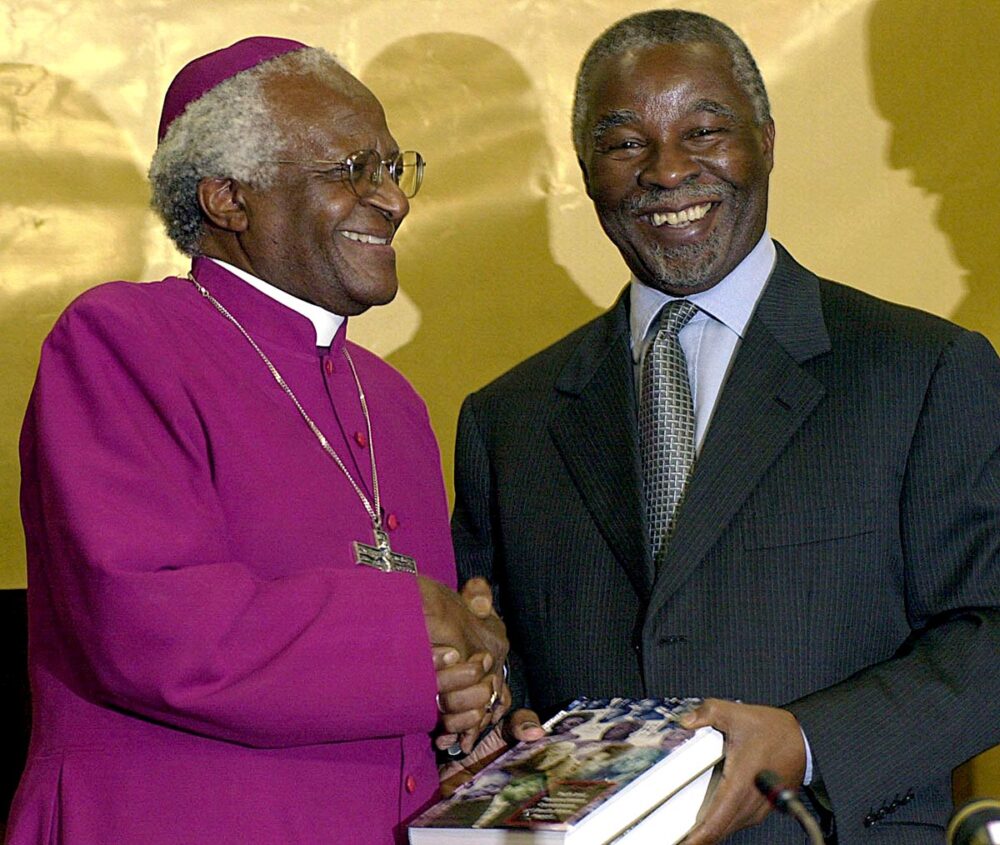 In South Africa, Archbishop Desmond Tutu presents the report of the Truth and Reconciliation Commission to South African President Thabo Mbeki on 21 March 2003 in Pretoria. The two personalities smile and shake hands.