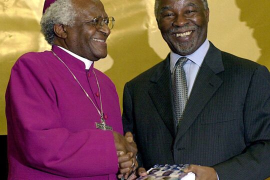 En Afrique du Sud, l’archevêque Desmond Tutu remet le rapport de la Commission vérité et réconciliation au président sud-africain Thabo Mbeki, le 21 mars 2003 à Pretoria. Les deux personnalités se serrent la main en souriant.