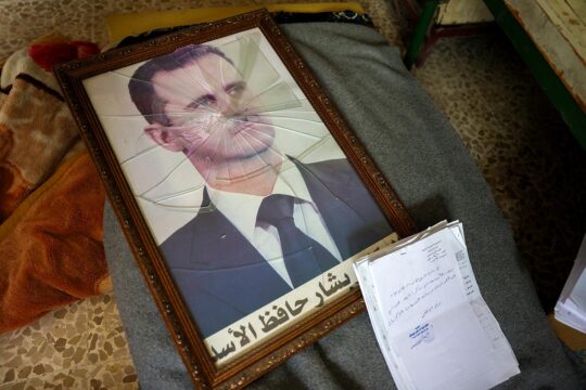 La justice internationale pour les crimes de Bachar el-Assad en Syrie. Photo : portrait brisé de Bachar el-Assad à côté de documents.