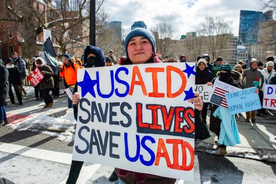 Suspension de l'aide américaine (USAID et autres subventions et organisations) : l'impact se ressent aussi sur la justice transitionnelle. Photo : une femme tient une pancarte où il est écrit : 