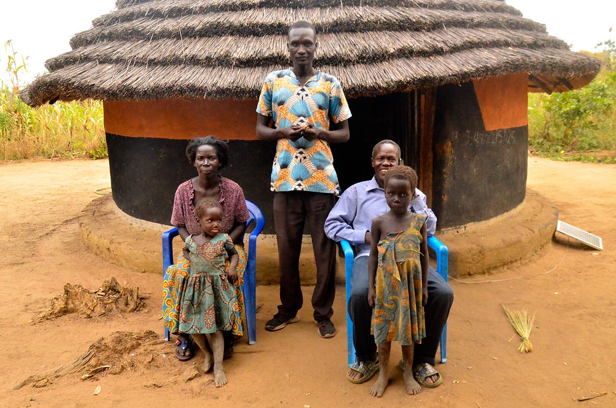 Reportage dans le village de naissance de Thomas Kwoyelo, en Ouganda, auprès de sa famille. Photo : des proches de Kwoyelo devant la maison où il a vécu enfant.