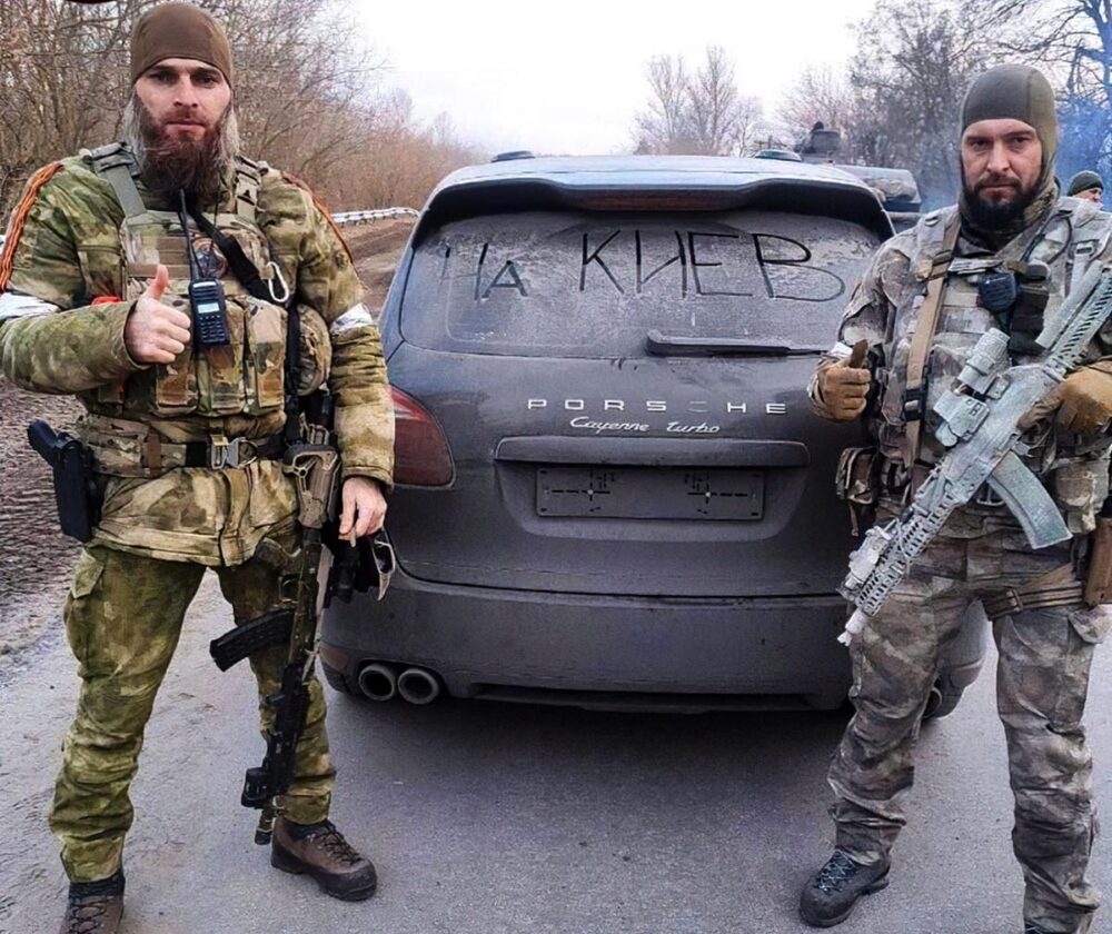 Daniil Martynov en Ukraine – Photo : Deux militaires armés posent (en levant le pouce) devant l'arrière d'une voiture de marque Porsche.