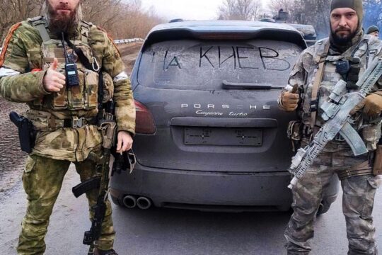 Daniil Martynov en Ukraine – Photo : Deux militaires armés posent (en levant le pouce) devant l'arrière d'une voiture de marque Porsche.