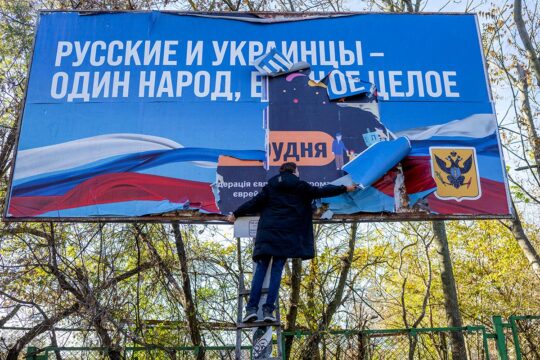 Procès pour collaboration en Ukraine. Photo : un homme retire l'affiche de propagande russe à Kherson au moment de sa libération par les forces armées ukrainiennes.