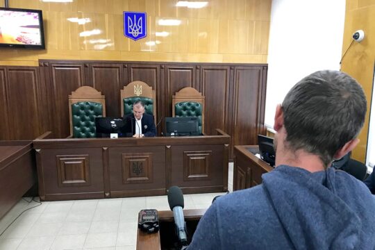 Procès contre des entrepreneurs privés jugés pour collaboration avec la Russie, en Ukraine. Photo : lors d'un procès en Ukraine, un témoin apparaît de dos, faisant face à un juge dans une petite salle d'audience.